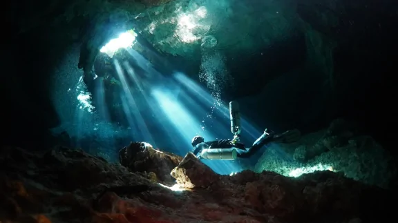 divers inside tropical cave, some light shine through holes in the cave ceiling